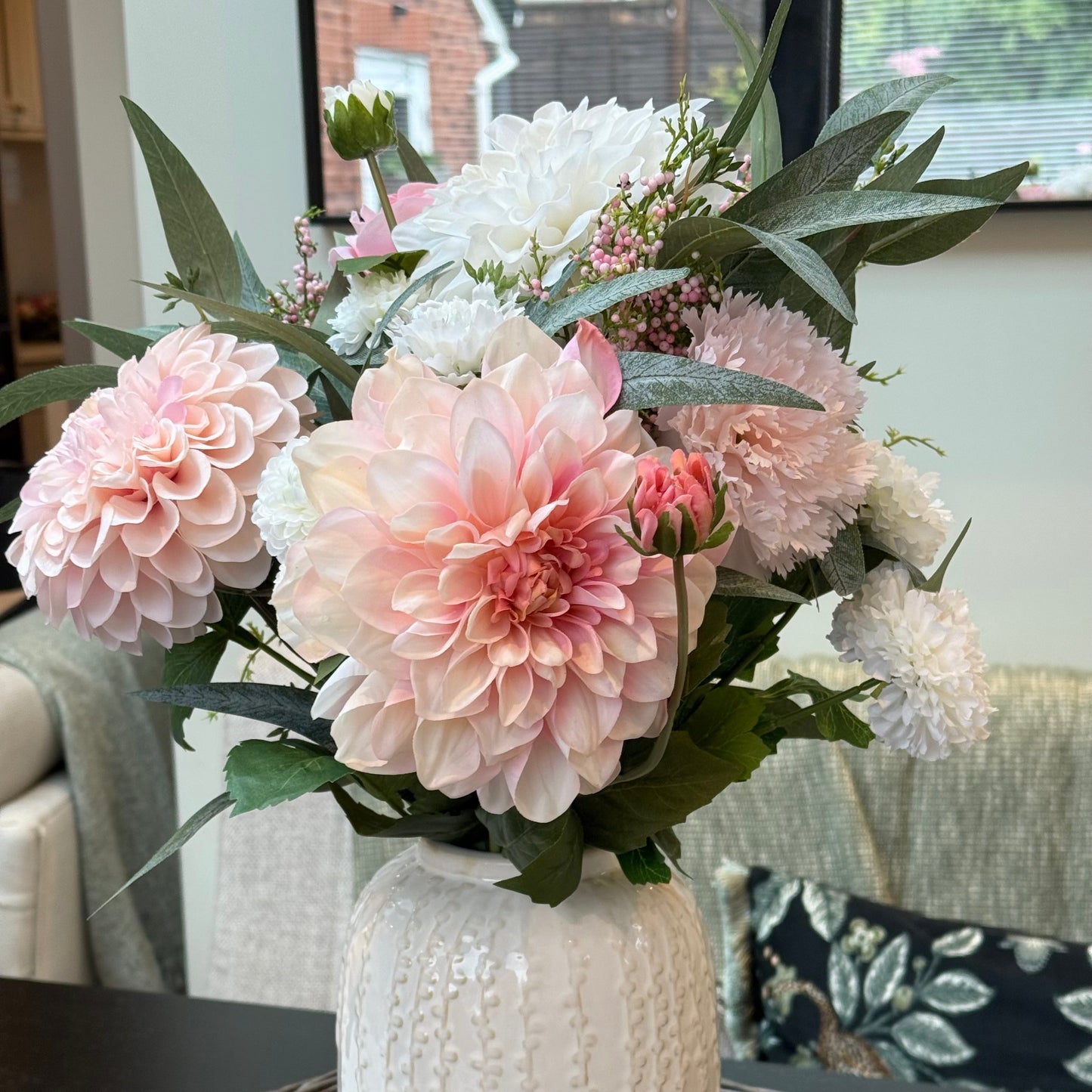 Bouquet of pink and white flowers in a textured white vase on a woven surface.