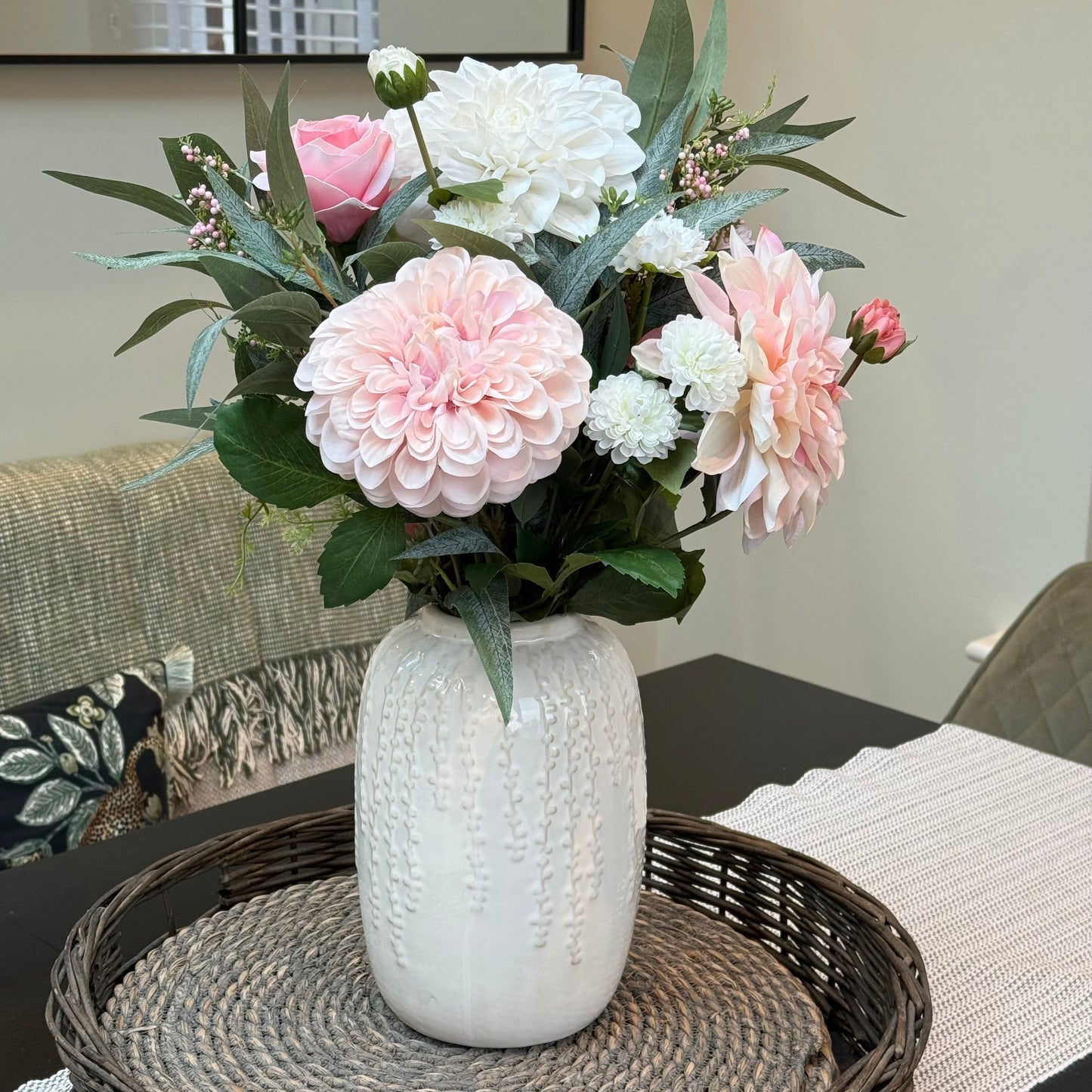 Floral arrangement in a white vase on a table with a blurred background
